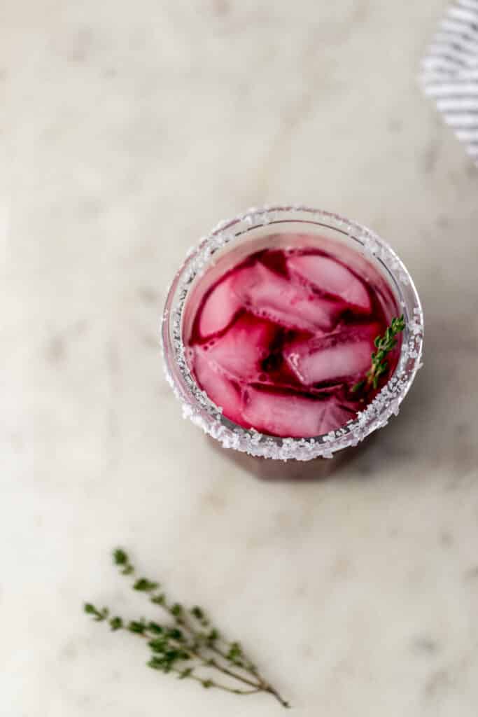 overhead view salt rimmed glass with blackberry margarita on ice in it. 