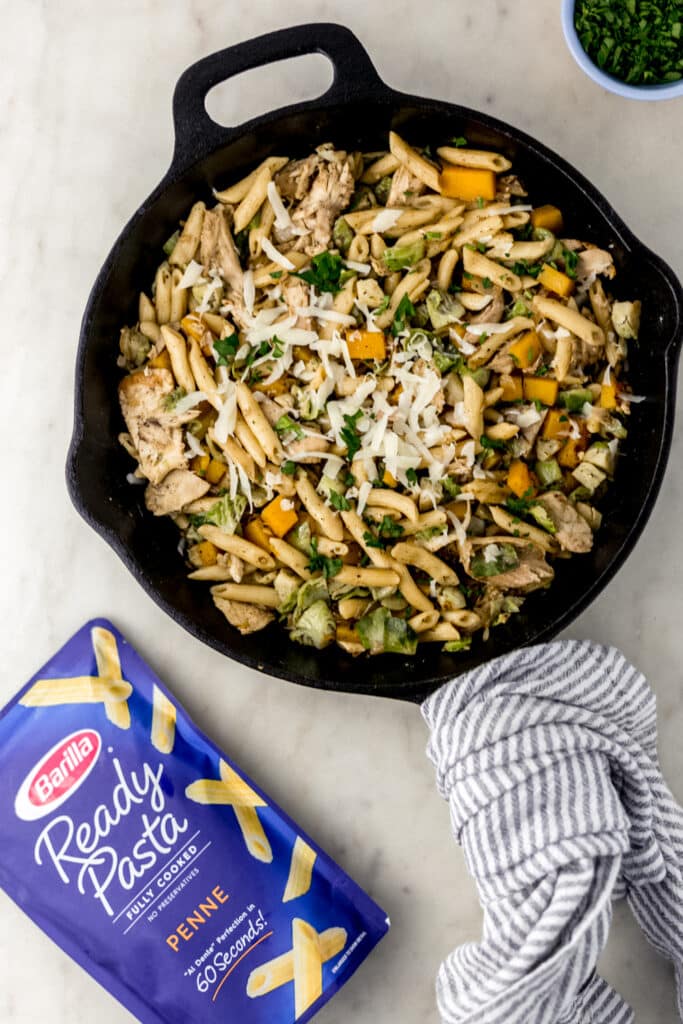 fall inspired pasta in cast iron skillet topped with parmesan cheese next to pasta packaging. 