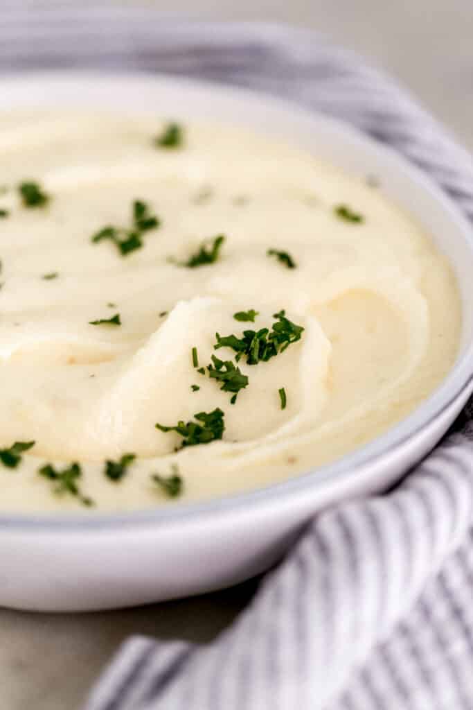 close up side view creamy mashed potatoes in white serving bowl topped with parsley. 