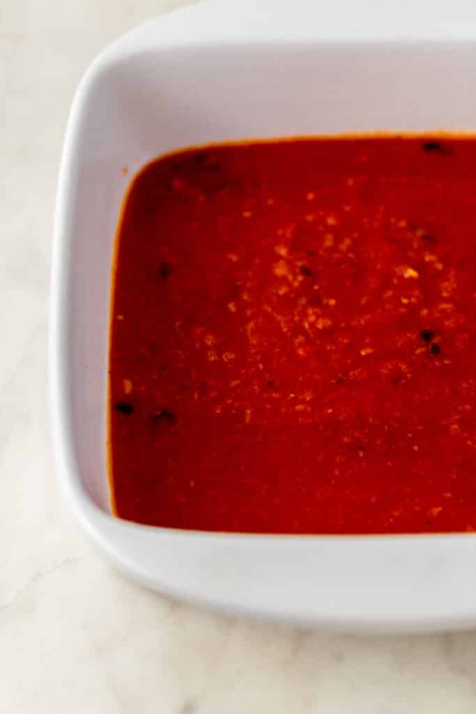 sauce spread evenly at the bottom of a white square baking dish 