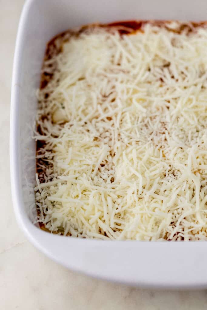 ravioli, sauce, and mozzarella layered in square white baking dish.