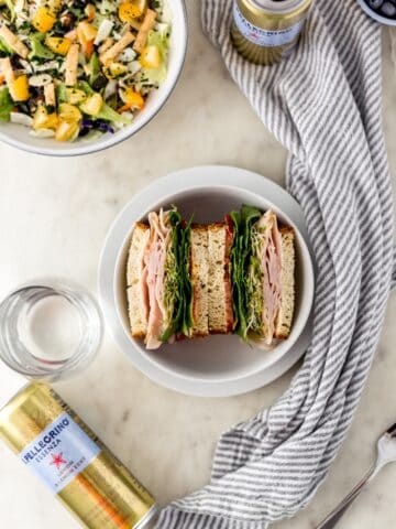 overhead view of sandwich in bowl, salad, drinks, and cloth napkin