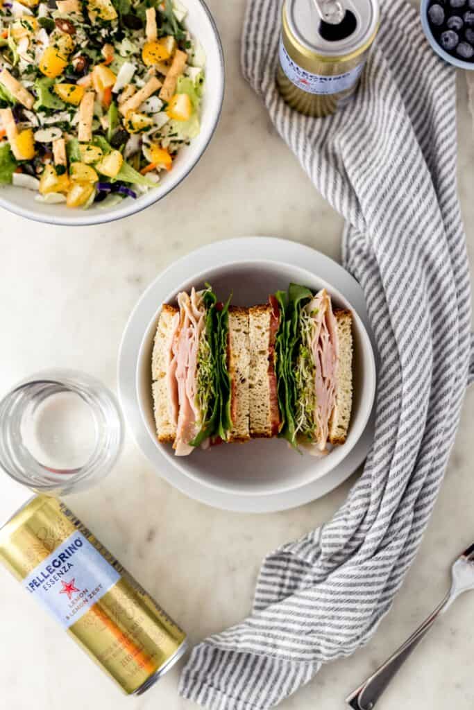 overhead view of sandwich in bowl, salad, drinks, and cloth napkin 