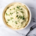 Overhead view of potatoes in white bowl topped with parsley.