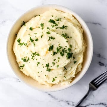 Overhead view of potatoes in white bowl topped with parsley.