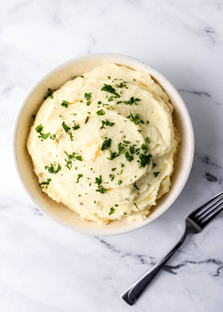 Overhead view of potatoes in white bowl topped with parsley.