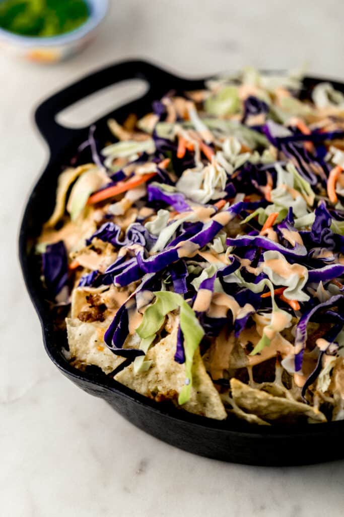 close up side view ground pork nachos in cast iron skillet topped with cole slaw and spicy mayo. 