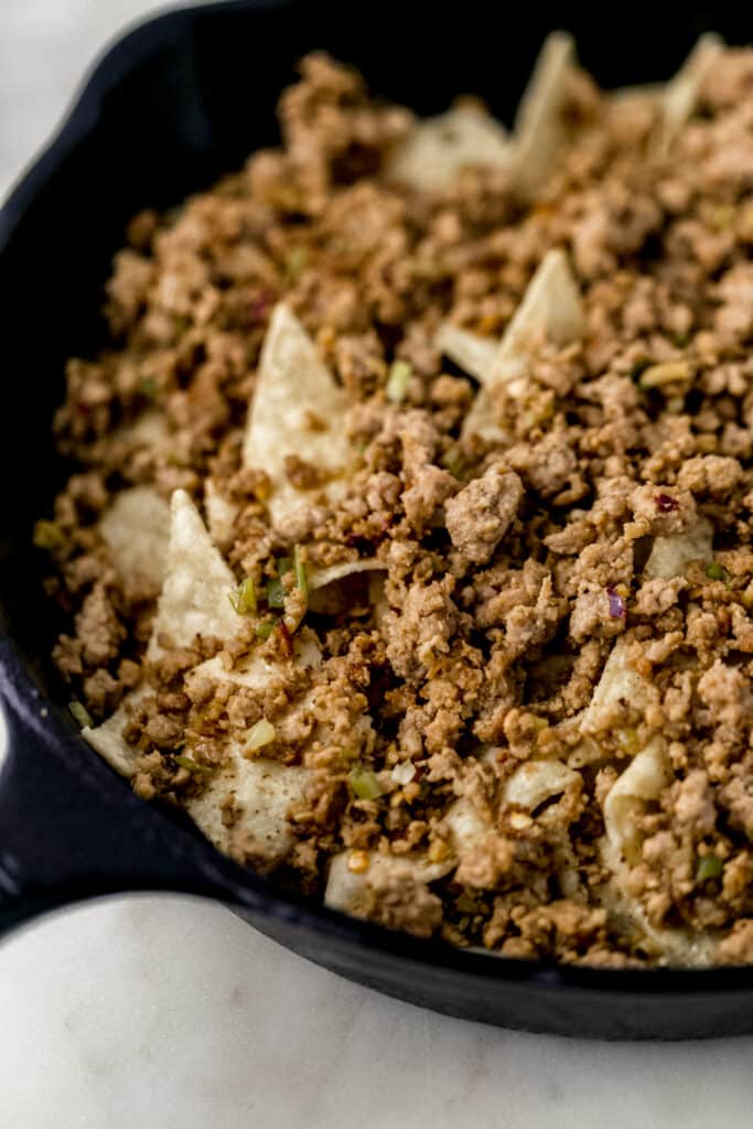 close up side view tortilla chips and ground pork in cast iron skillet