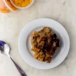 peach bread pudding on white plate beside a spoon