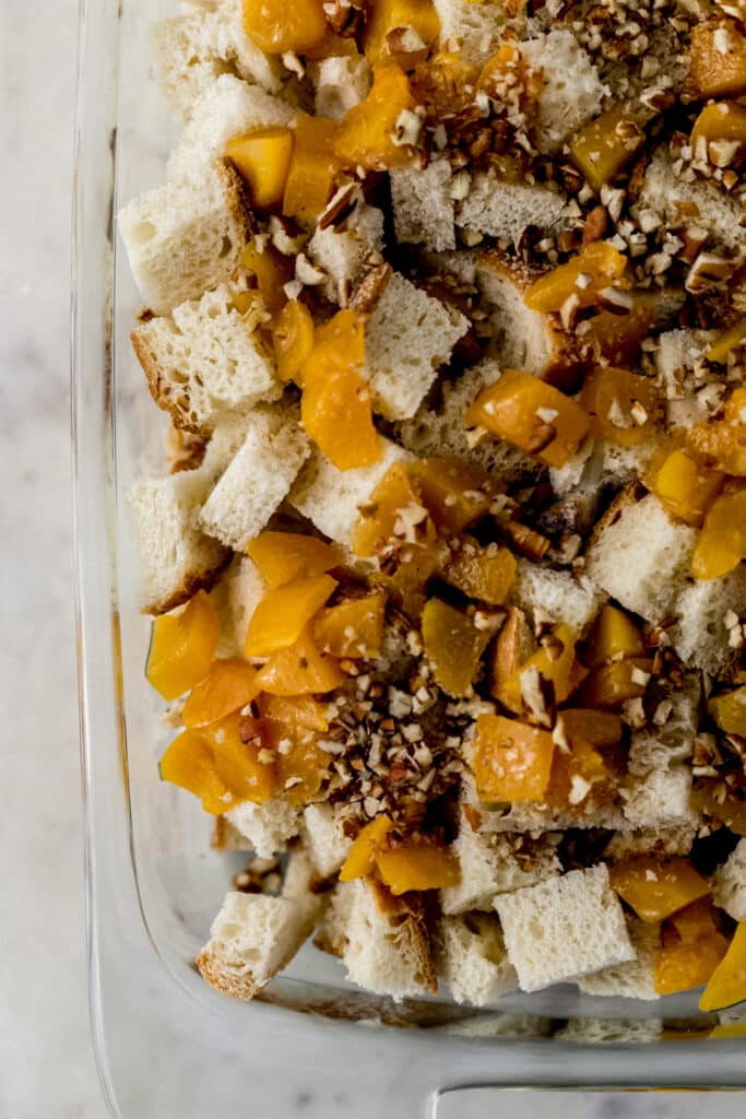 butter, bread, peaches, and pecans in rectangle baking dish