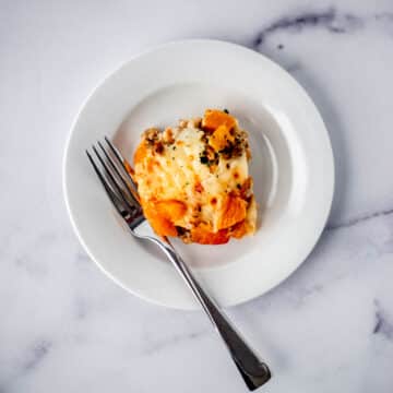 single serving of sausage and peach strata on white plate with fork.
