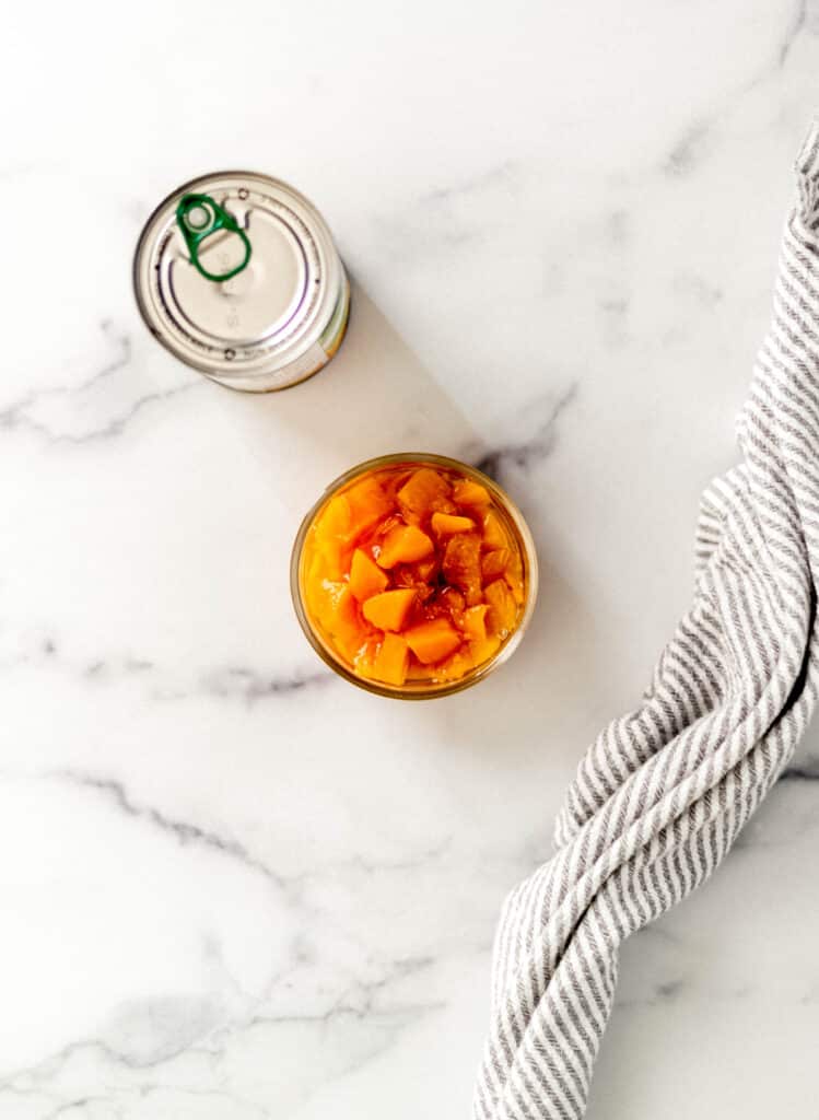 overhead view glass bowl with diced peaches in it next to a can