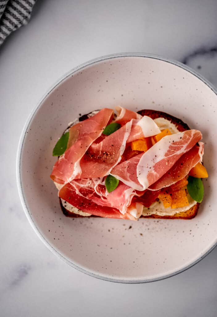 toast topped with prosciutto and peaches in white bowl