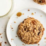 Single cookie on white plate by glass of milk.