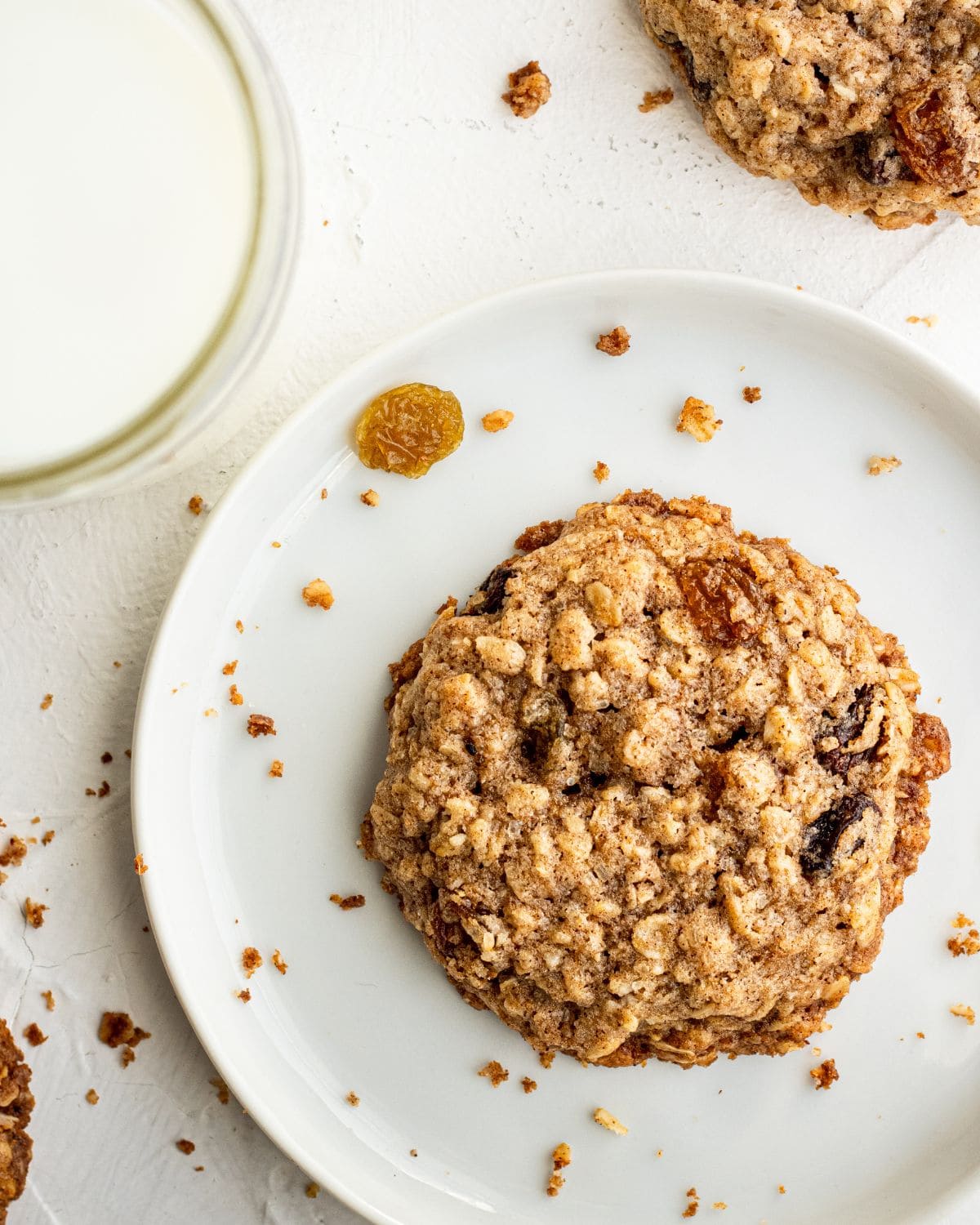 Overhead view of cookie on white plate by glass of milk. 