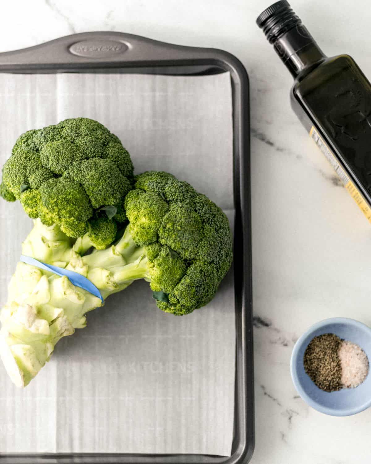 Overhead view of ingredients needed to make broccoli on marble surface. 