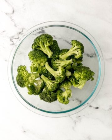 Overhead view of cleaned and cut broccoli florets in a glass bowl.