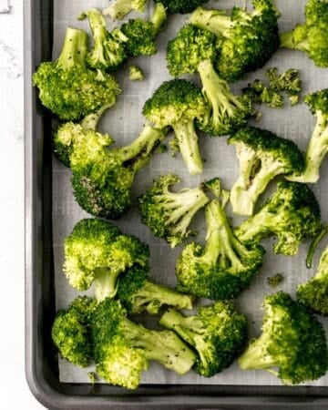 Seasoned raw broccoli on a parchment lined sheet pan.