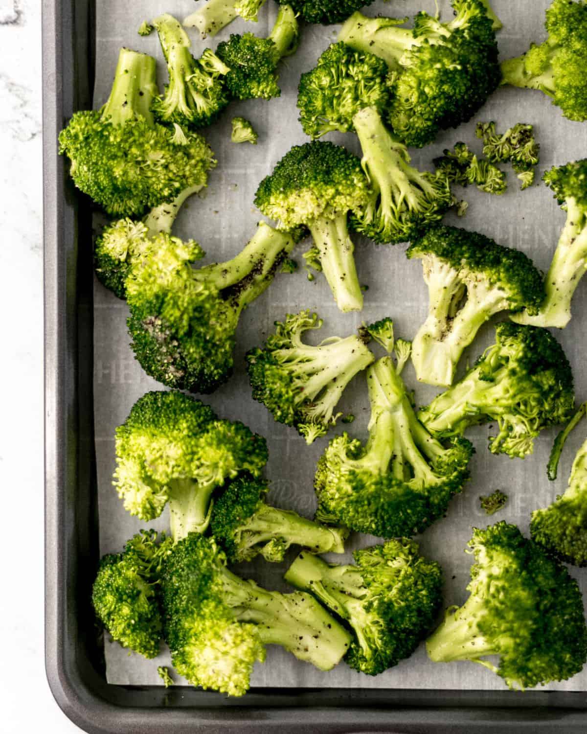 Overhead view of seasoned broccoli on parchment lined sheet pan. 