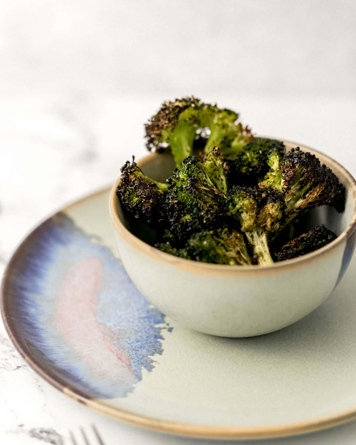 Close up of side view of finished broccoli in small bowl on top of matching plate. 