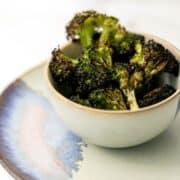 Close up side view of finished broccoli in small grey bowl on top of plate.