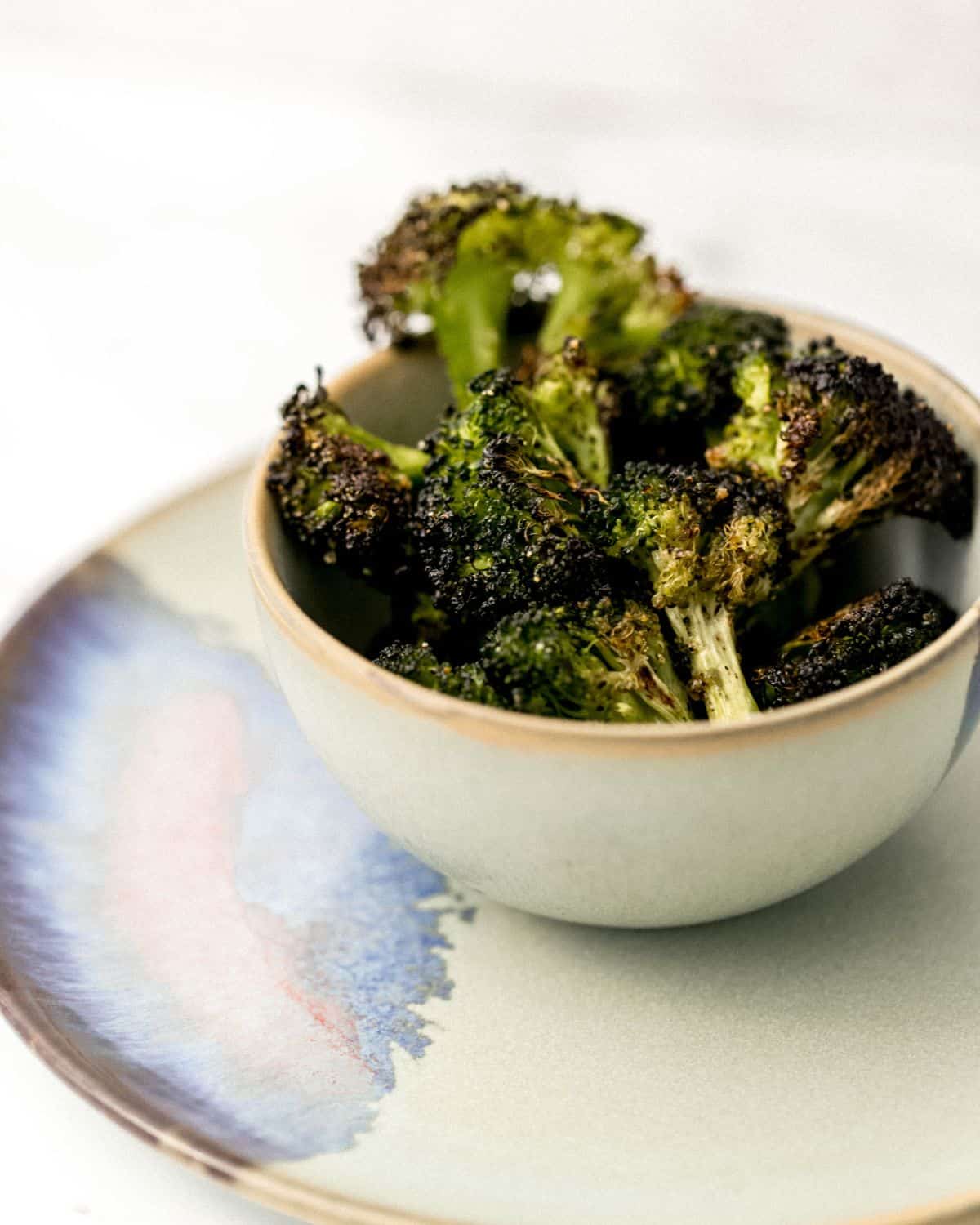 Close up side view of finished broccoli in small bowl on top of plate.