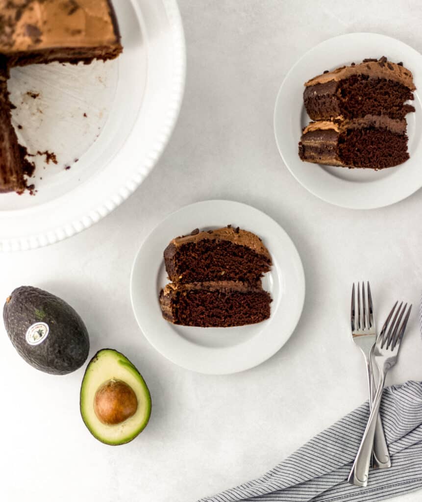 slices of chocolate cake on white plates beside avocados and forks