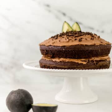 chocolate cake on white cake stand beside avocados