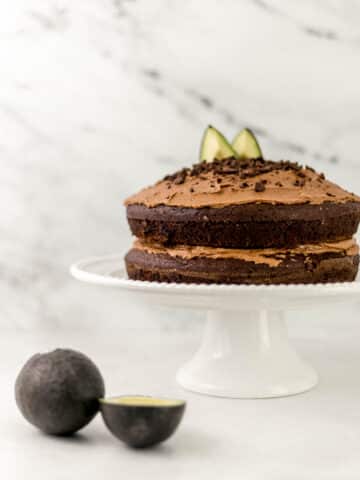 chocolate cake on white cake stand beside avocados
