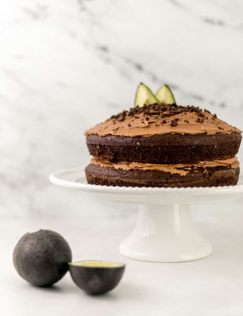 chocolate cake on white cake stand beside avocados 