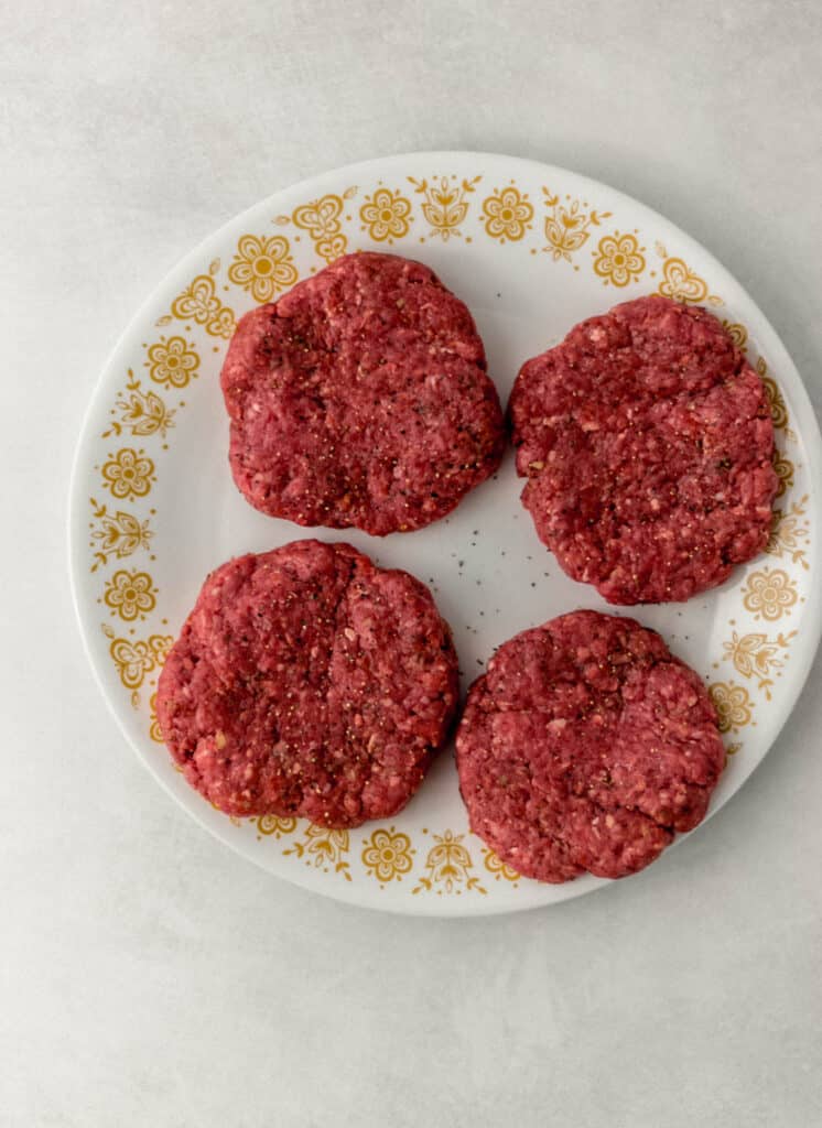 raw hamburger patties on white decorative plate. 