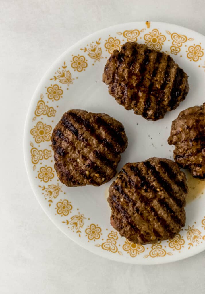 four grilled burgers on white decorative plate. 