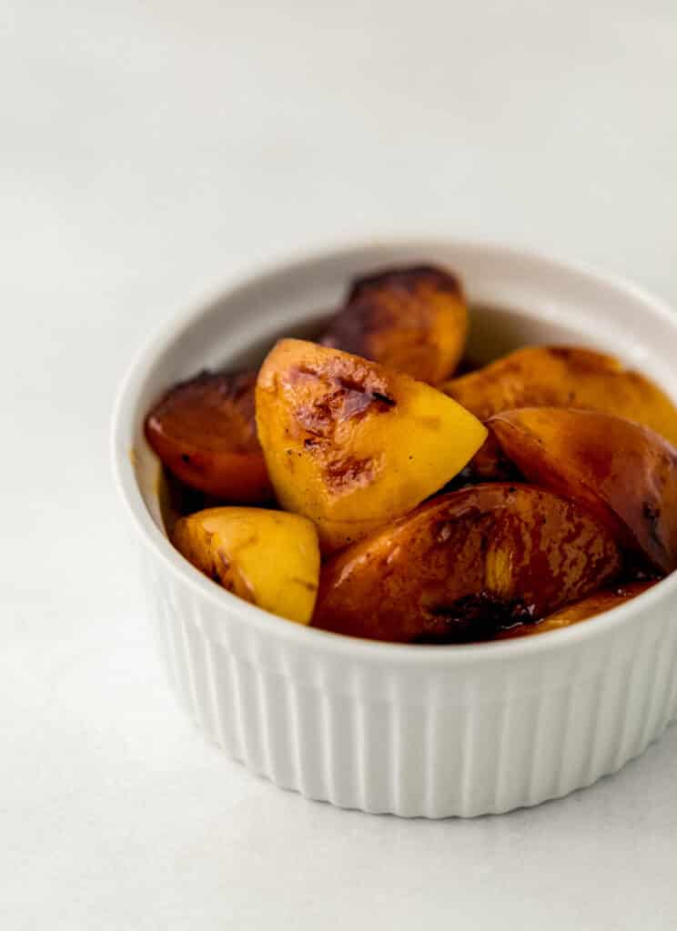 close up side view grilled peaches in white bowl. 