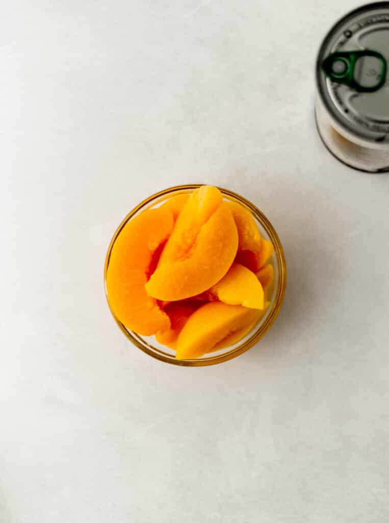 sliced peaches in small glass bowl next to can of unopened peaches. 