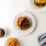 hamburger on white plate with small glass bowl of grilled peaches