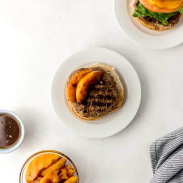 hamburger on white plate with small glass bowl of grilled peaches