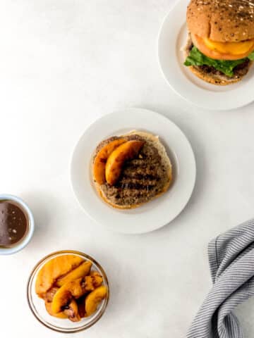 hamburger on white plate with small glass bowl of grilled peaches
