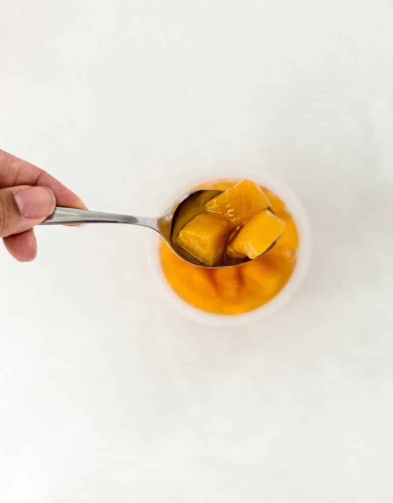 hand holding spoon with diced peaches on it over container