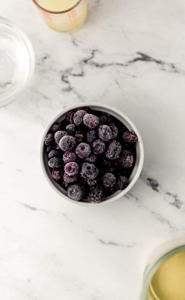 overhead view small white bowl with frozen blueberries in it along with other ingredients around it. 