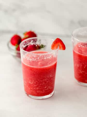 two margaritas in glasses with small glass bowl of fresh strawberries.