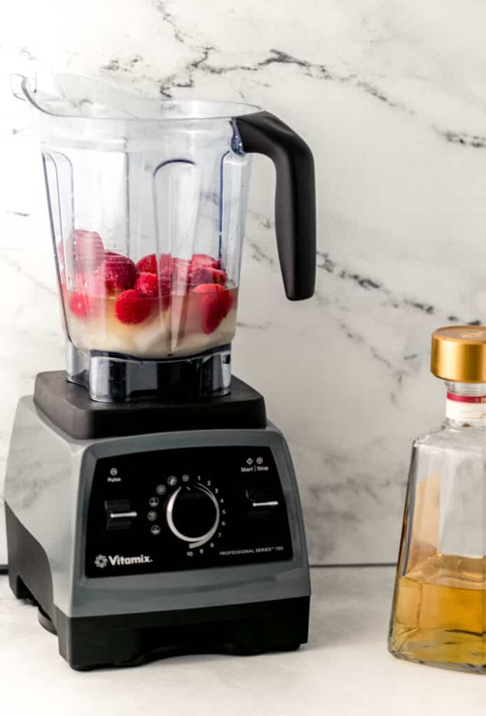 blender with ingredients to make margarita in it beside a bottle of tequila. 