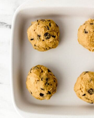 Four cookie dough balls in square white baking dish.