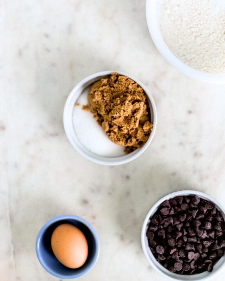Overhead view of ingredients to make cookies in separate bowls on marble surface.