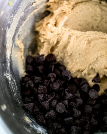 Chocolate chips added to cookie mixture in stand mixer bowl.