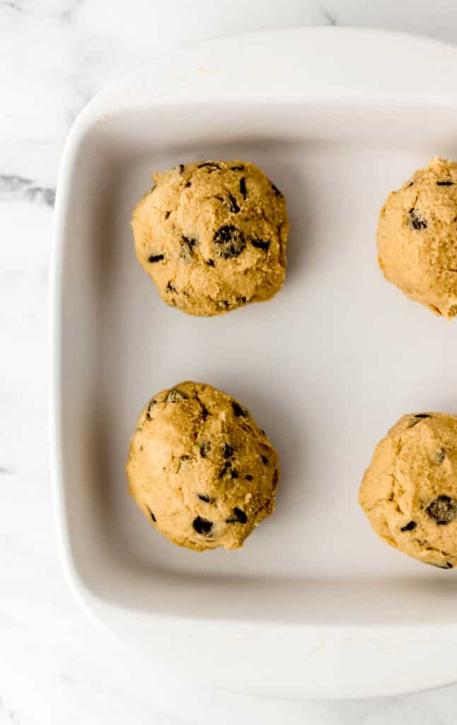 four balls of cookie dough in white square baking dish