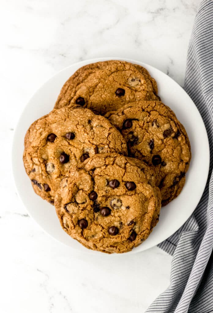 white plate with four large cookies on it beside cloth napkin on marble surface