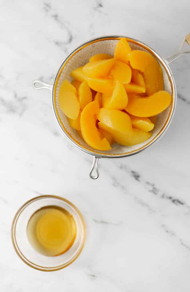 strainer with sliced cling peaches and small glass bowl with honey.