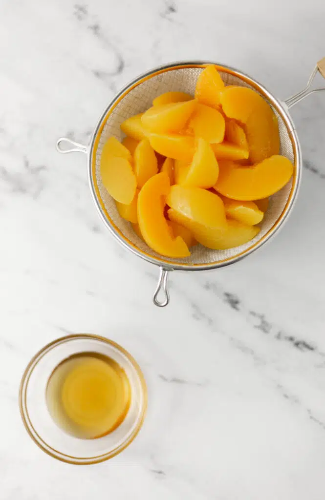 strainer with sliced cling peaches and small glass bowl with honey. 