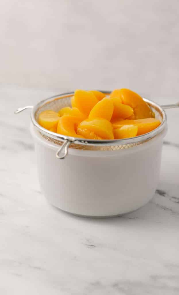 side view white bowl topped with strainer with sliced peaches in it draining
