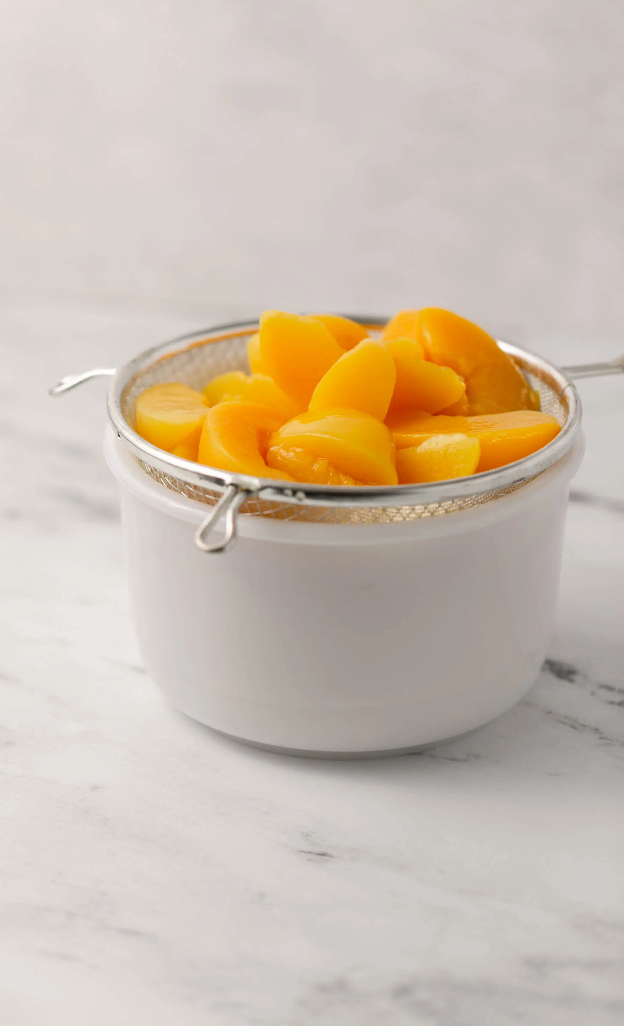 sliced peaches draining in a strainer over a white bowl
